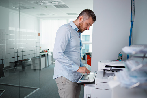 Man standing by the photocopier in the office and programming number of copies on touch screen panel