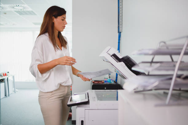 istock Female office clerk looking at document and putting it in xerox 1343123918