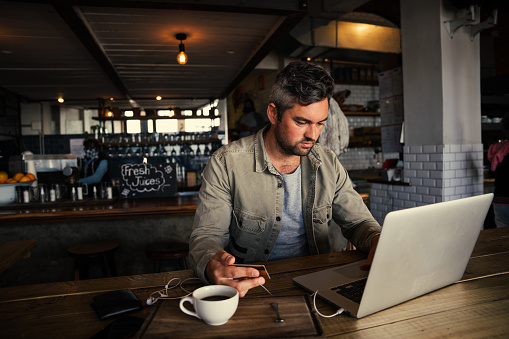 Stressed caucasian businessman making online payment with card while working on laptop drinking coffee in trendy cafe. High quality photo