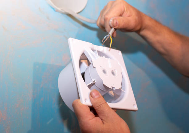 Man is installing the wall bathroom fan vent. Restoration process. Wires in hands. Maintenance repair works renovation in the flat.
