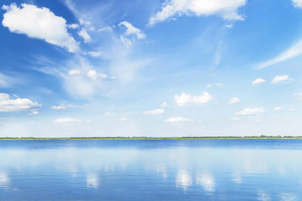 istock Blue sky with light clouds soft focus, trees and reflection in the water in the sunny summer day. 1343136320