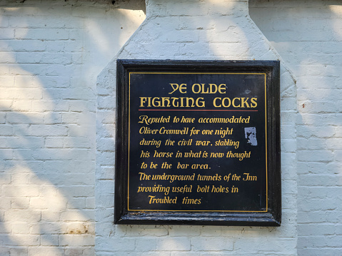 The weathered sign for the 'Ye Olde Fighting Cocks' pub, allegedly the oldest pub in England. St Albans, Hertfordshire, England, UK. This  is outside the pub entrance. The pub was originally located close to St Albans Cathedral (when it was St Albans Abbey) and was moved to the present site sometime around 1539. The foundations are claimed to be even older, dating from around 793 but this is unconfirmed.