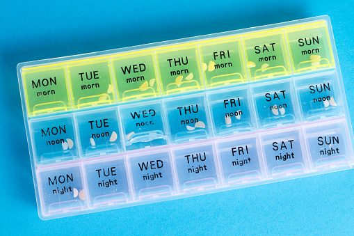 Organizer for medical pills on a blue isolated background close-up. Organization of taking pills of the day.