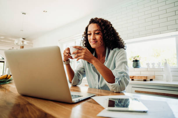 istock Mixed race female student working from home drinking hot coffee looking at laptop 1343149936