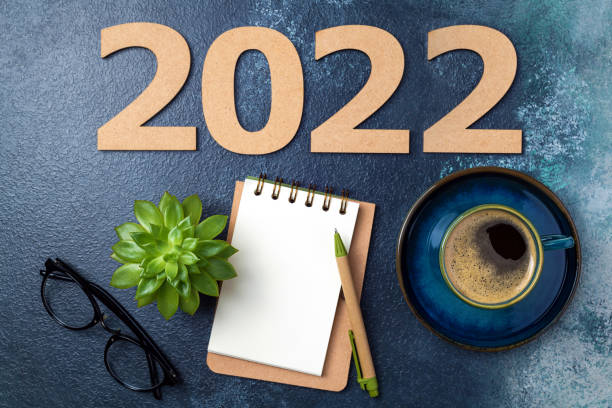 istock New year 2022 Resolutions and notebook on desk. 2022 template with open notebook, coffee cup, eyeglasses, succulent on blue background. Goals, plan, strategy, resolutions, business concept 1343150139
