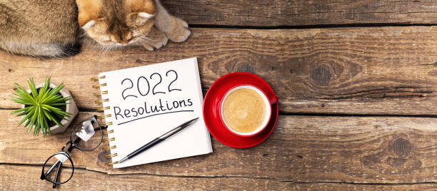 istock New year Resolutions 2022 on desk. 2022 resolutions with notebook, cute cat, coffee cup, eyeglasses, succulent on wooden table. Goals, plan, list, idea, cozy home concept 1343150168
