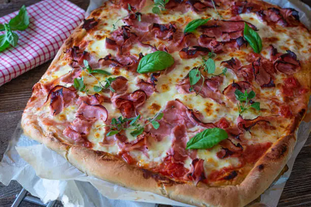 Delicious traditional italian pizza with Prosciutto cotto, mozzarella cheese and tomato sauce. Served on rustic and wooden table. Closeup