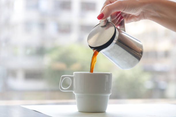 istock Woman's hand holding a coffee mug and pouring it into the coffee cup. Morning routine lifestyle concept, close up 1343150659