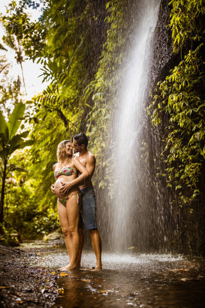 istock Happy pregnant couple talking under the waterfall in rainforest. 1343156908