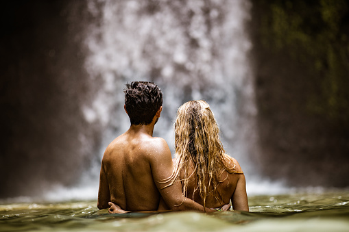 Back view of a couple looking at waterfall from water in nature. Copy space.