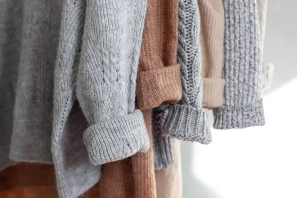 Photo of Pastel warm knitted clothes sweater hanging in the closet. Cozy autumn and winter wardrobe.
