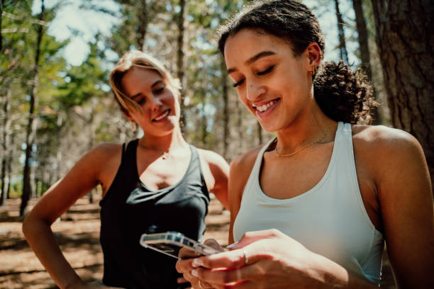 istock Two female friends standing together in forest texting on cellular device smiling 1343165179