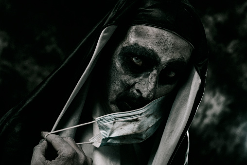 a scary evil nun, in a black and white habit, covers her mouth with a dirty disposable face mask