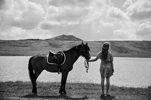 Beautiful young woman with a horse by the lake
