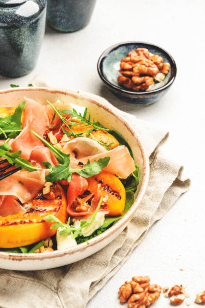 istock Salad bowl with grilled peach, prosciutto, goat cheese, walnuts and arugula on white background, top view, copy space 1343179393