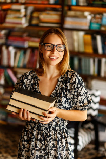 istock Back to school library concept. Student girl holding book on her hands on background of bookshelves in the library. Education and school concept 1343181201