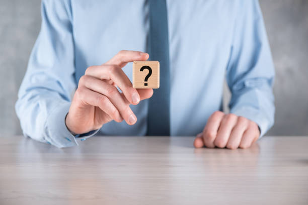 istock Businessman hold and put wooden cube block shape with question marks on grey table. Space for text.concept for confusion, question or solution 1343188264