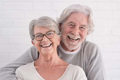 Cheerful couple of two beautiful senior people hugging each other - standing having fun at home - serene retirement concept
