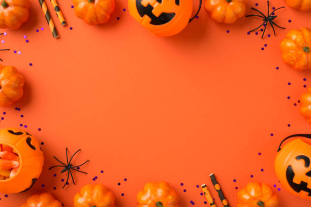 istock Top view photo of halloween decorations violet sequins pumpkin baskets with candy corn spiders and straws on isolated orange background with blank space in the middle 1343189341