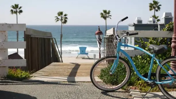 Blue bicycle, cruiser bike by ocean beach, pacific coast, Oceanside California USA. Summertime vacations sea shore. Vintage cycle by wooden stairs, stairway or staircase. Tropical palms and lifeguard