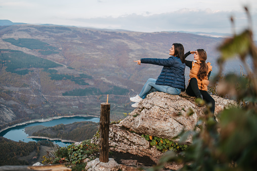 Side view of a hikers looking at view from rocky mountain while one friend is aiming at distance. The other one with her hand on a forehead is peering into distance. Kozji kamen, Stara planina