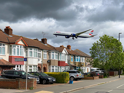 London, United Kingdom, May 16, 2021:  A British Airways passenger aircraft flying over the rooftops of the houses on the landing approach to Heathrow Airport in London, UK.  Myrtle Avenue is a street in the London Borough of Hounslow which is near the eastern end of Heathrow airport's south runway, 27L. This makes it especially noisy when aircraft are landing or taking off from 27L, though its view of the aircraft has made it the prime location for plane spotting.
