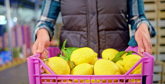 Mid section of woman holding crate of fresh lemons in warehouse.