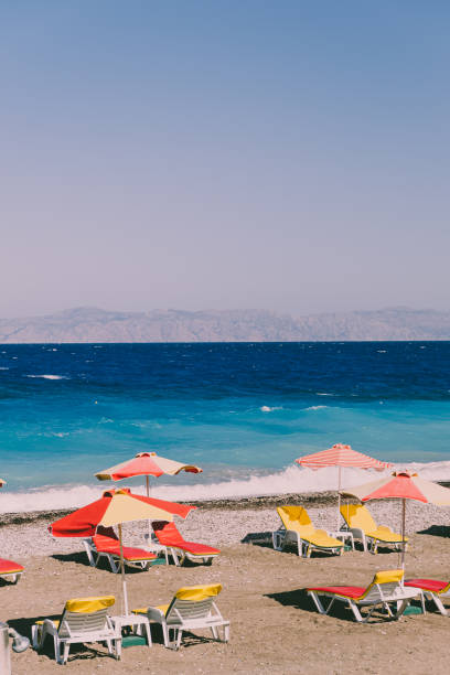 strand mit gelben und roten sonnenliegen, sonnenschirmen und meer mit wellen. konzept im retro-stil. schöne aussicht auf die landschaft - greek revival style stock-fotos und bilder