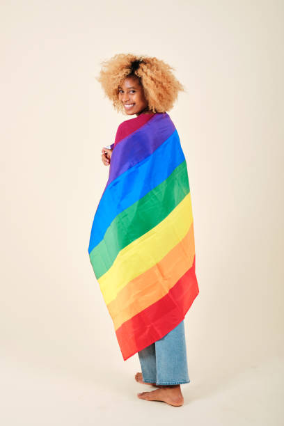 istock Woman looking into camera and smiling while wrapped with a lgbt pride flag on an isolated background. 1343225539