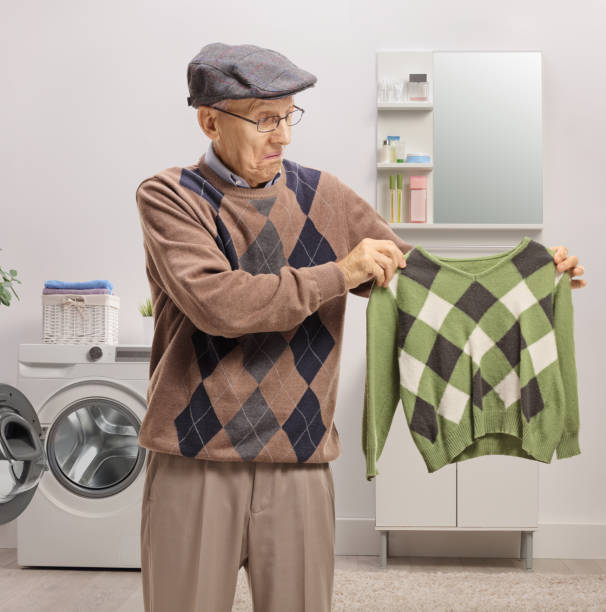 Disappointed elderly man holding a shrunken blouse Disappointed elderly man holding a shrunken blouse in a bathroom contracting stock pictures, royalty-free photos & images