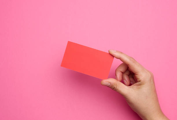 istock Female hand holding empty  red paper on a pink background. Copy paste image or text 1343240358