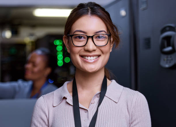 beschnittenes porträt einer attraktiven jungen programmiererin, die in einem serverraum mit ihrer kollegin im hintergrund arbeitet - data center computer programmer women stock-fotos und bilder