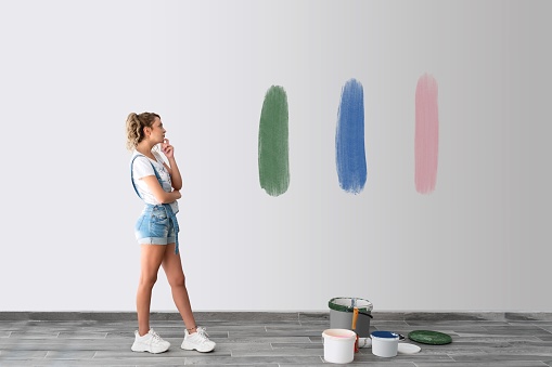 Beautiful woman is standing front of the wall and try to decide the color of painting wall. High quality photo