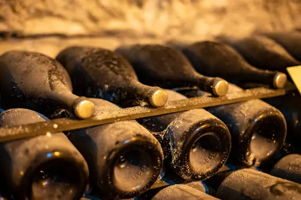 Walking in deep and long undergrounds caves with dusty bottles on racks, making champagne sparkling wine from chardonnay and pinor noir grapes in Reims, Champagne, France