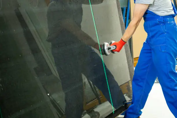 An employee in a glass factory places a large sheet of glass on a specialized, automatically lifted table using professional suction cups