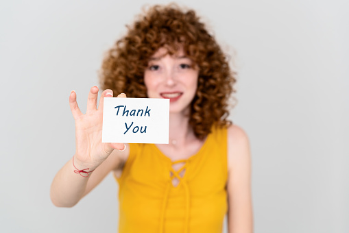 Young red hair woman is holding a paper with a Thank you note. Silent communication concept. High quality photo