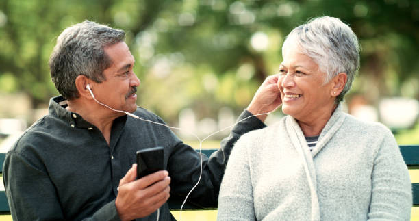 shot of an elderly couple listening to while sitting on a bench in a garden - using phone garden bench imagens e fotografias de stock