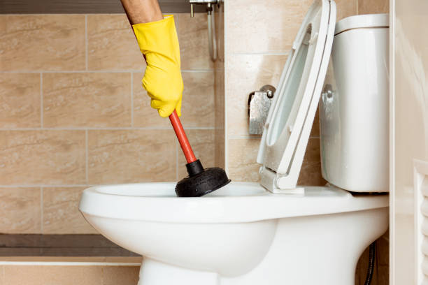 Human hand wearing yellow rubber gloves is using a device to fix a clogged toilet bowl. stock photo
