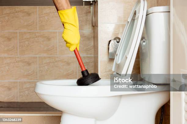 Human Hand Wearing Yellow Rubber Gloves Is Using A Device To Fix A Clogged Toilet Bowl Stock Photo - Download Image Now