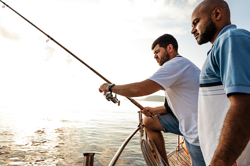 Two young men standing on sailboat with fishing rod fishing and looking at haul