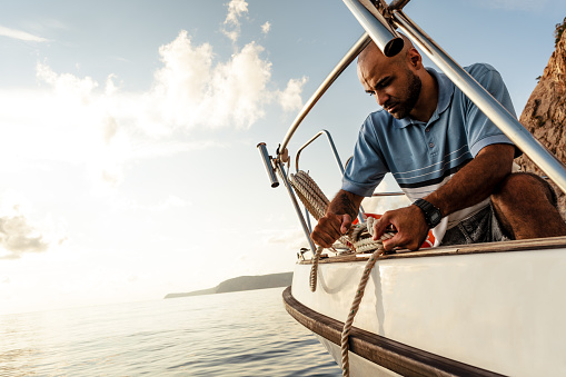 Joven marinero afroamericano atando cuerdas en velero en el mar al atardecer photo