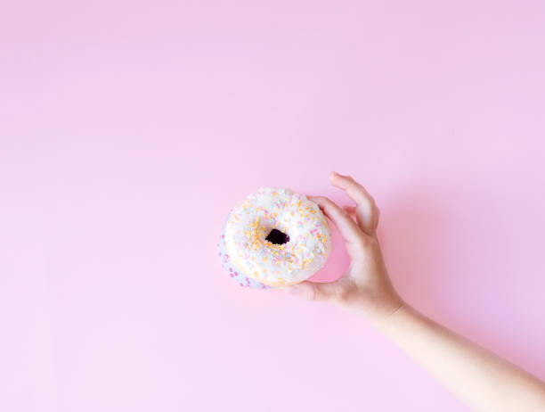 istock donuts on a pink background. Hand holds donut 1343275223