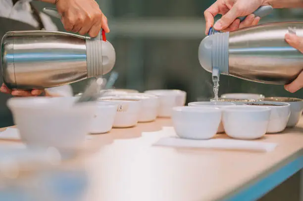 close up professional Asian Chinese barista grader pouring hot water in ceramic coffee cup preparing for coffee cupping coffee quality test