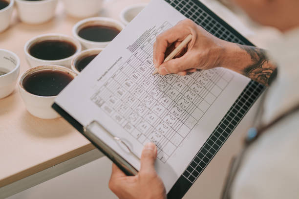 Close up professional Asian Chinese barista connoisseur performing coffee cupping writing down on clipboard after tasting coffee cupping Close up professional Asian Chinese barista connoisseur performing coffee cupping writing down on clipboard after tasting coffee cupping taste test stock pictures, royalty-free photos & images