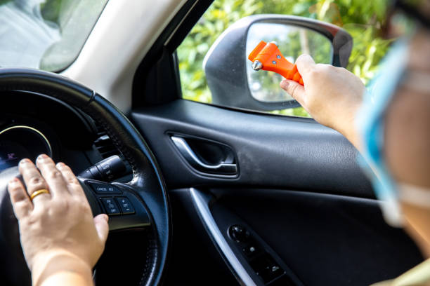 女性は車の中で安全ハンマーとシートベルトカッターを使用し、緊急時にガラスを割ります。車の安全赤いハンマーで緊急の場合は、草の窓を壊します。 - broken window glass women ストックフォトと画像