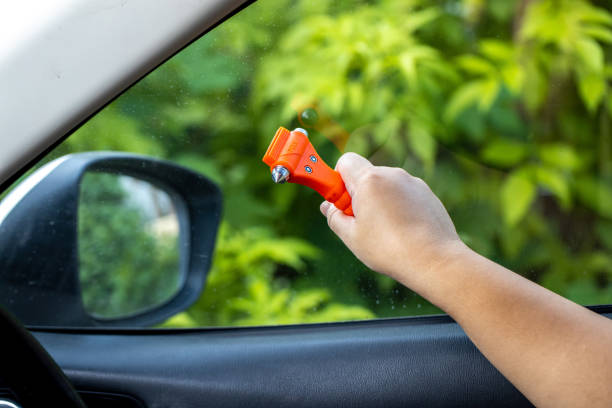 女性は車の中で安全ハンマーとシートベルトカッターを使用し、緊急時にガラスを割ります。車の安全赤いハンマーで緊急の場合は、草の窓を壊します。 - broken window glass women ストックフォトと画像