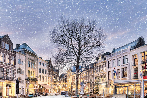 Winter view with snowfall of central historic square Plaats with bars and restaurants decorated with christmas lights in the ancient city center of The Hague, The Netherlands