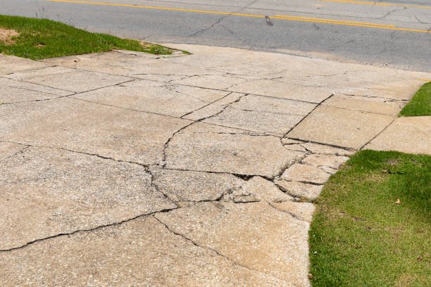 garagem de concreto agregado rachada e quebrada descendo em uma estrada asfáltica, ladeada por áreas verdes gramadas, espaço de cópia criativa - cracked - fotografias e filmes do acervo