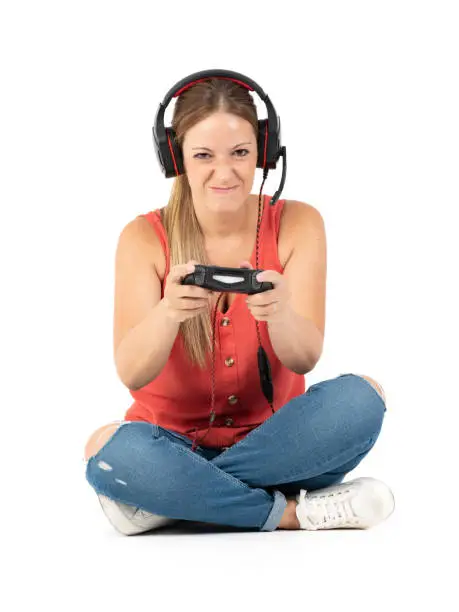 Young woman playing videogames with a controler and a headphones in a white background with jeans, white shoes and red shirt.