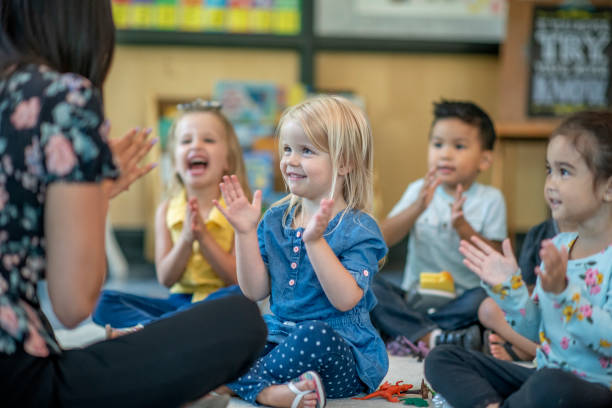 Preschool Children Singing Together A small group of multi-ethnic preschool children sit on the floor in front of their teacher as she teaches them a song.  They are each dressed casually and sitting with their legs crossed as they clap and sign along. nursery school child stock pictures, royalty-free photos & images